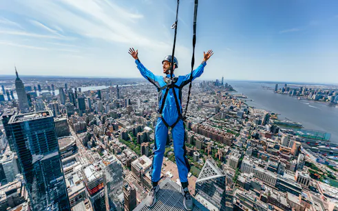 Person harnessed on skyscraper edge overlooking New York City skyline.