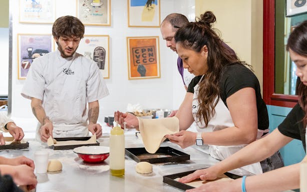 Participants making pizza and tiramisu in a Rome kitchen cooking class.