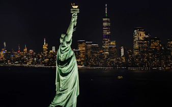 Statue of Liberty with New York City skyline at night.