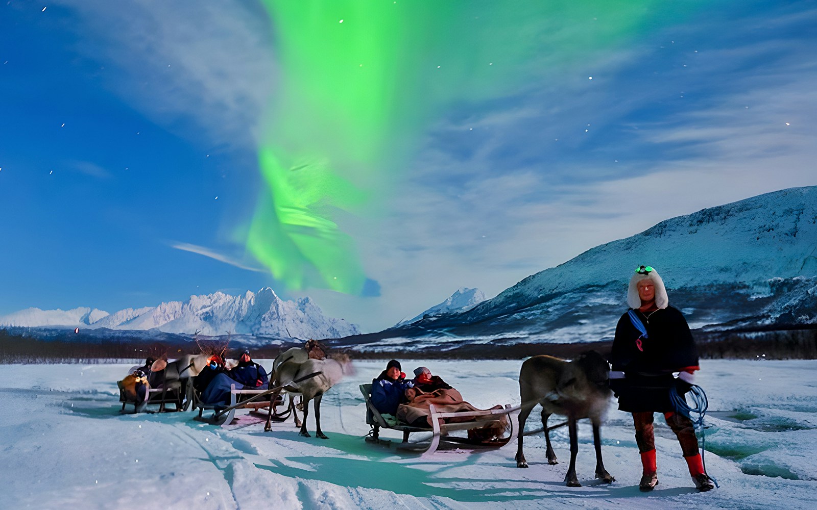 Tourists on reindeer sleds under Northern Lights in Tromso, Norway.