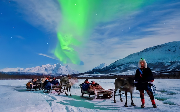 Tourists on reindeer sleds under Northern Lights in Tromso, Norway.