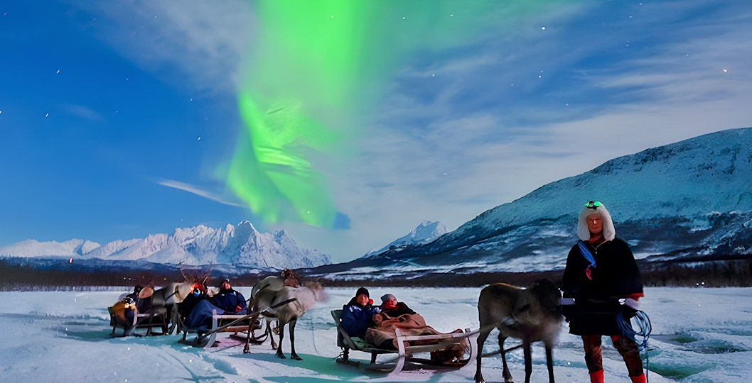 Tourists on reindeer sleds under Northern Lights in Tromso, Norway.