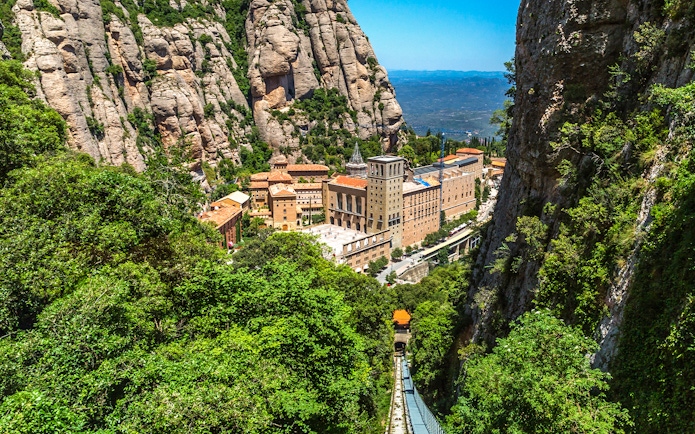 Montserrat monastery nestled in rocky mountains with funicular railway in foreground.