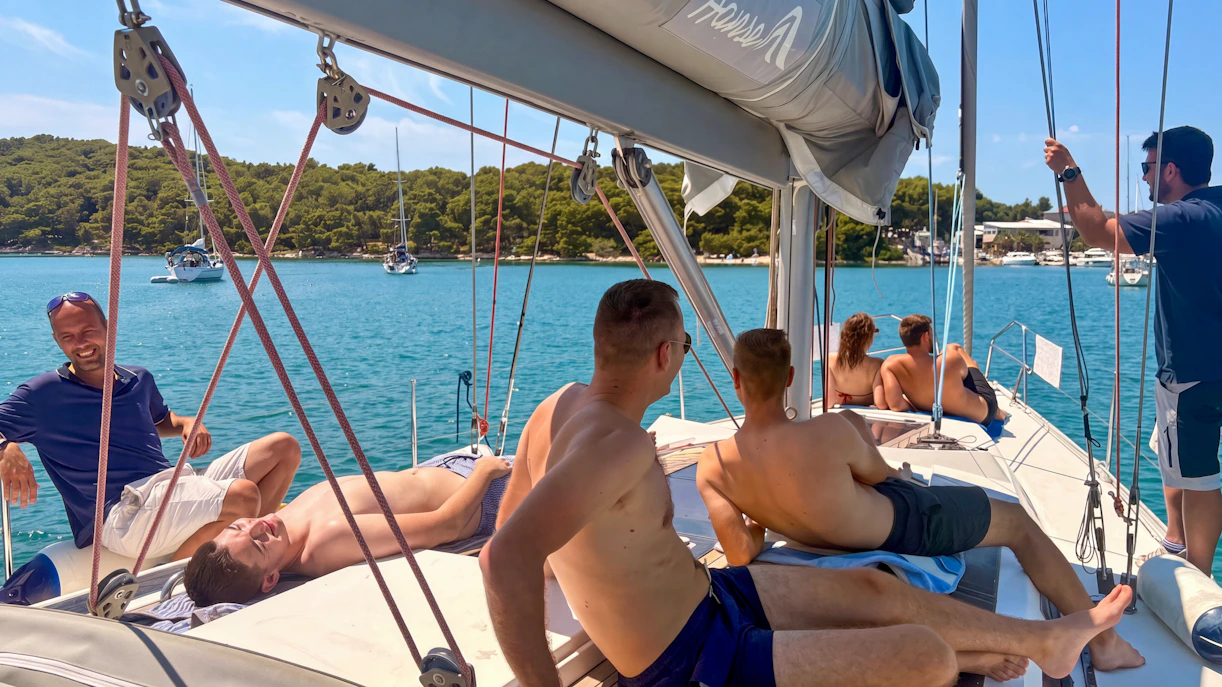 Sailing group relaxing on deck near Pula, Croatia, with scenic coastline in background.