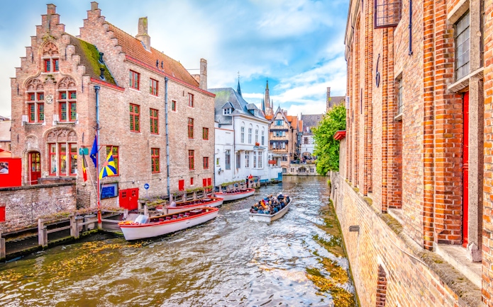 Boat trip on Bruges canal with historic brick buildings and tourists.