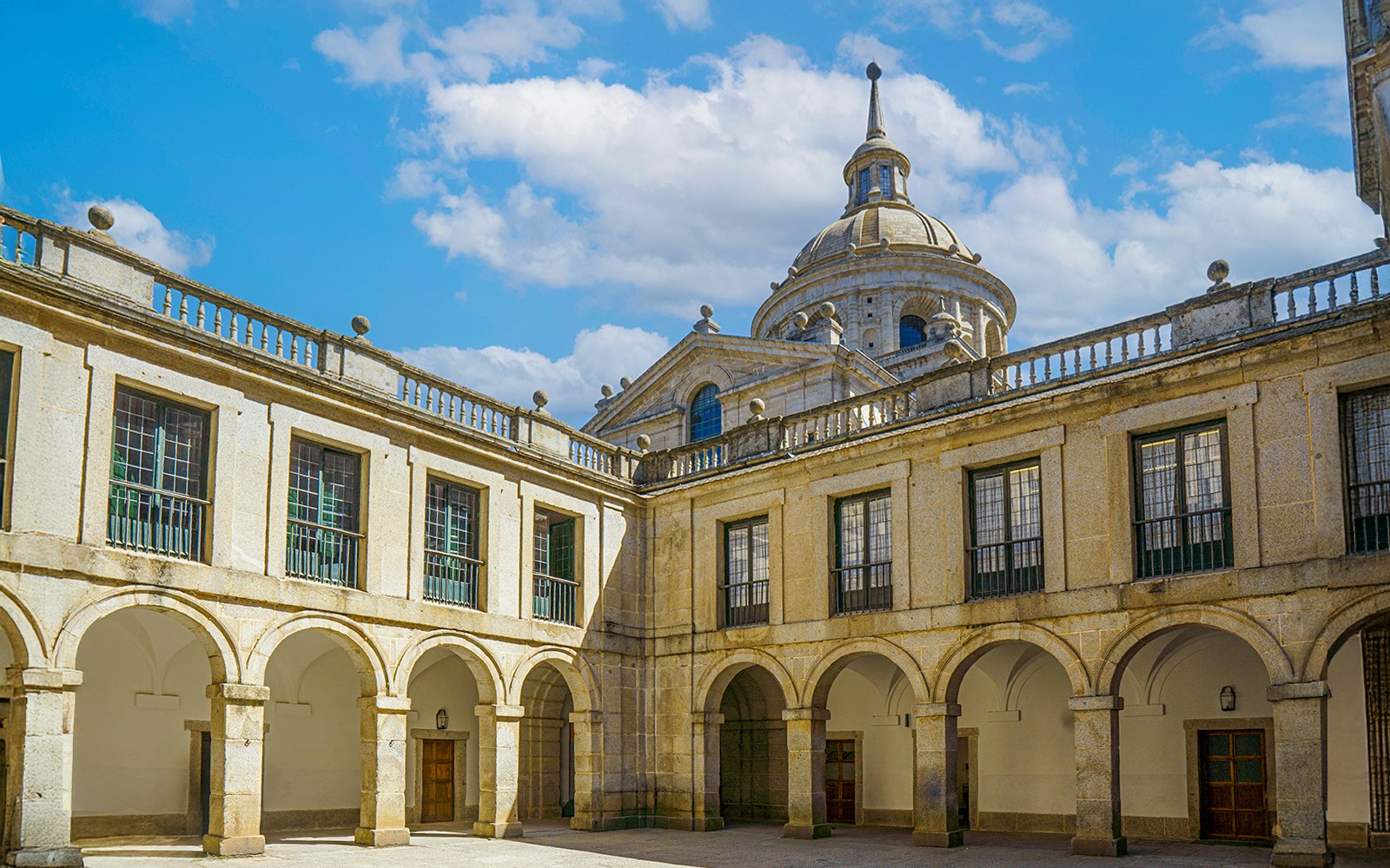 Courtyard of the Royal Monastery of San Lorenzo del Escorial, featuring historic architecture and stone arches.