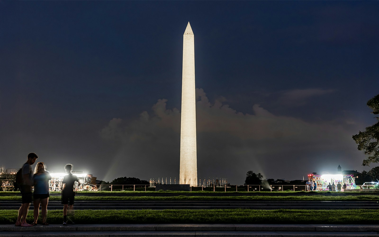 Washington Monument illuminated at night with visitors nearby.