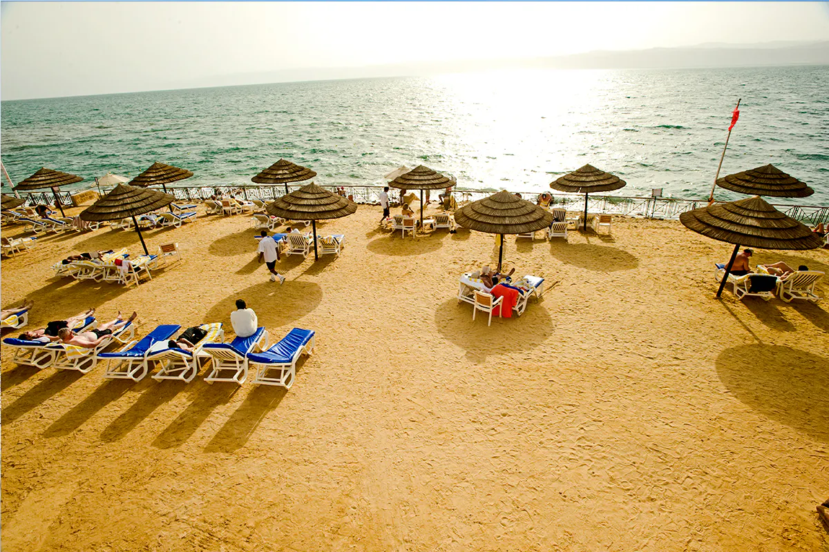 Beachgoers relax under umbrellas by the Dead Sea, Amman, during a half-day trip.
