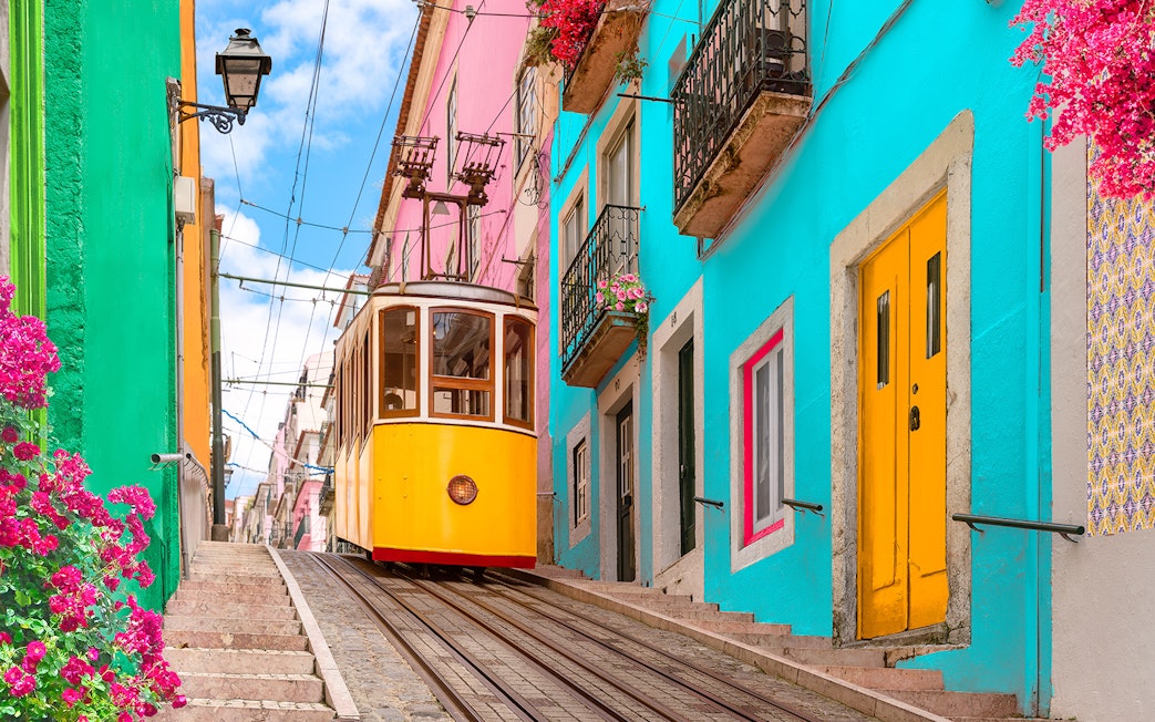 Lisbon tram on a steep street with colorful buildings and flowers.