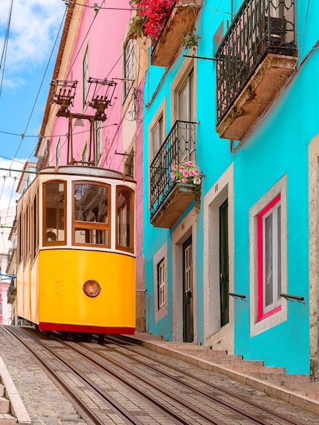 Lisbon tram on a steep street with colorful buildings and flowers.