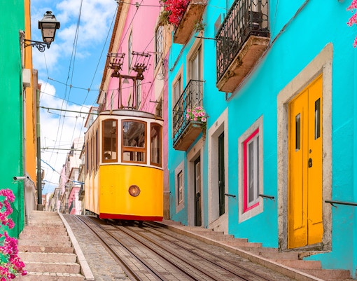 Lisbon tram on a steep street with colorful buildings and flowers.