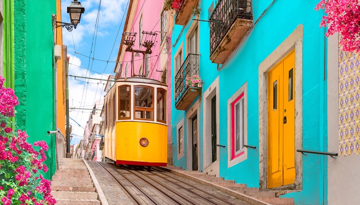 Lisbon tram on a steep street with colorful buildings and flowers.