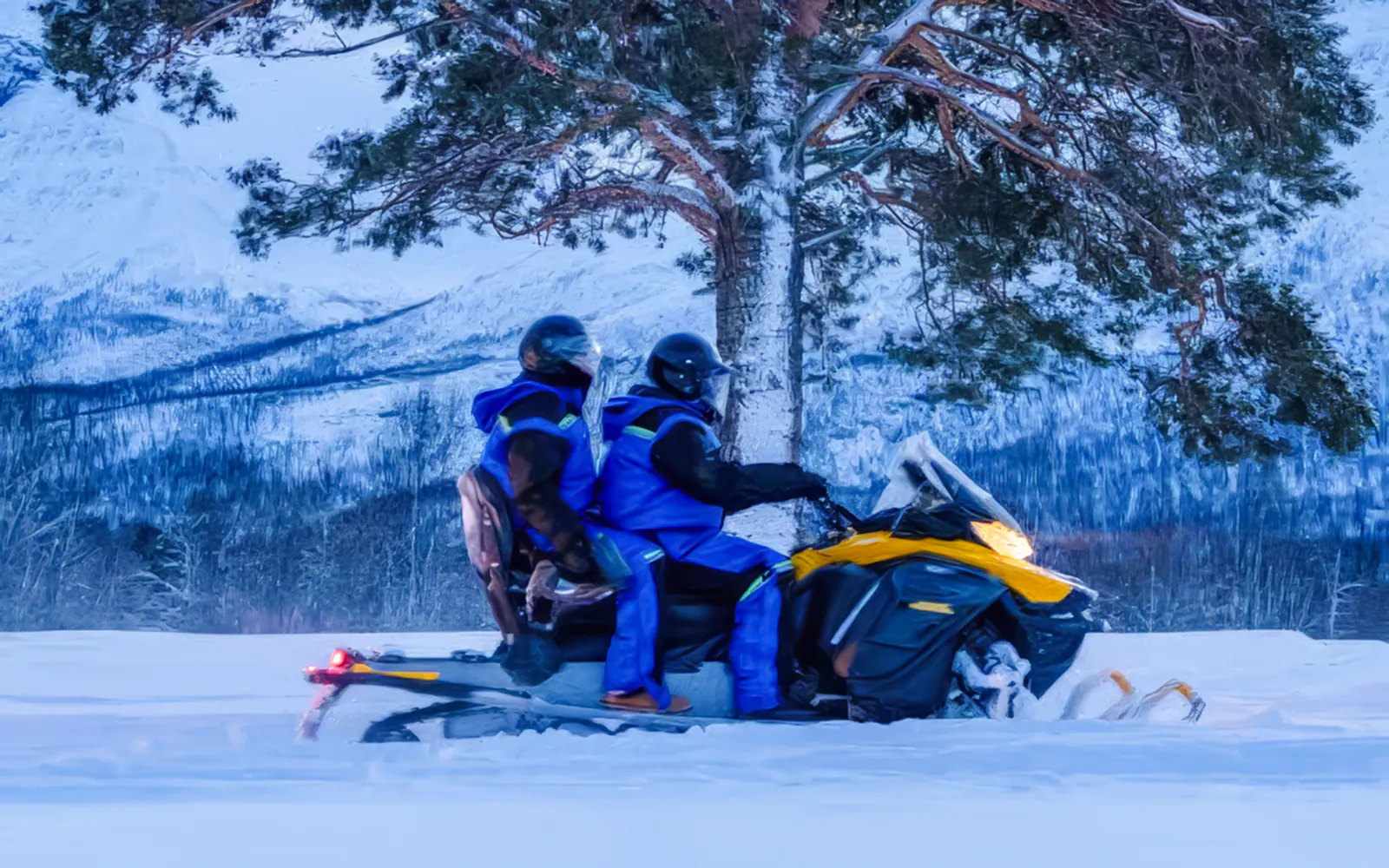 Two people riding a snowmobile through snowy landscape near Tromso.