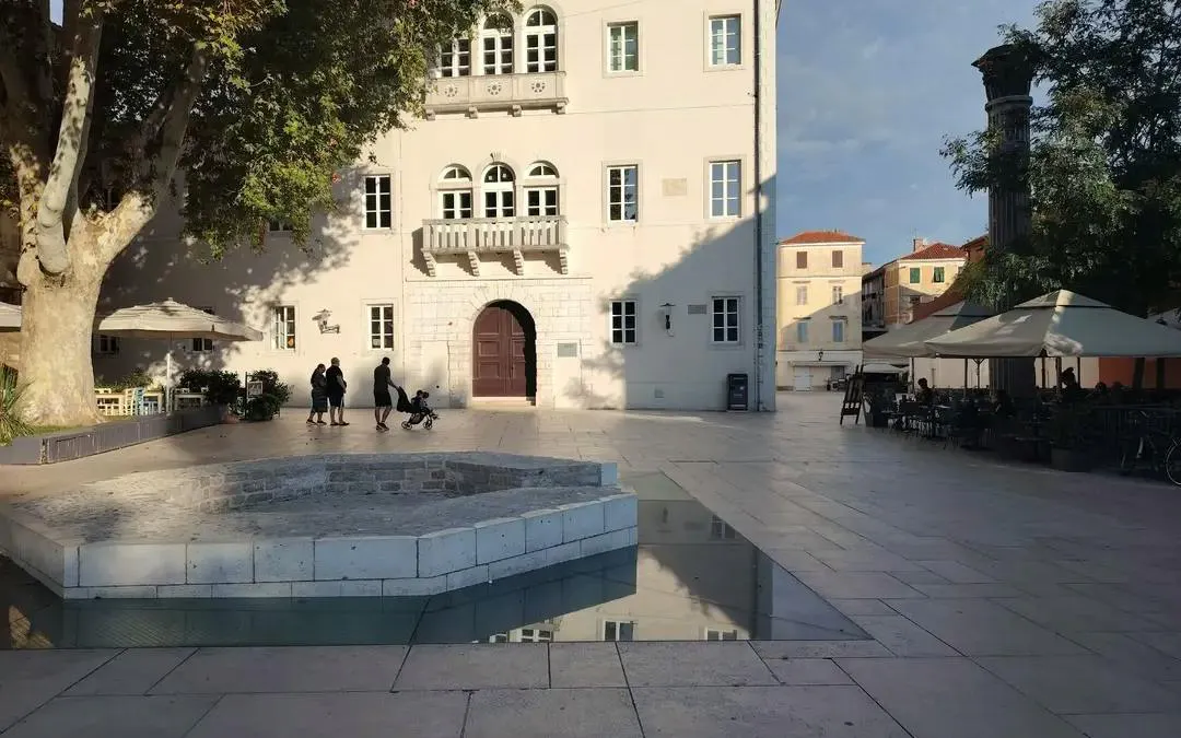 Zadar city square with historic building and people walking, part of self-guided exploration game.