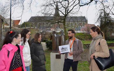 Tour guide explaining WWII history to group in Haarlem park near statue.