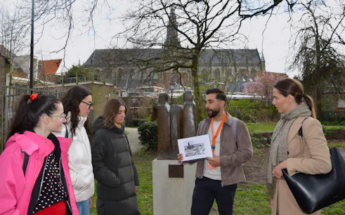Tour guide explaining WWII history to group in Haarlem park near statue.