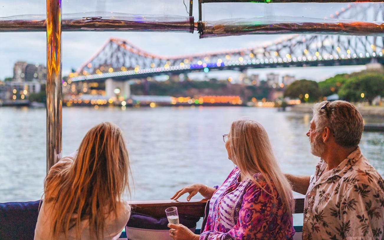 Passengers enjoy the view of the illuminated Story Bridge from a Brisbane River cruise at dusk.