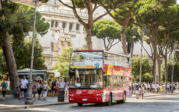 Rome sightseeing bus near Trevi Underground entrance, surrounded by tourists and historic architecture.
