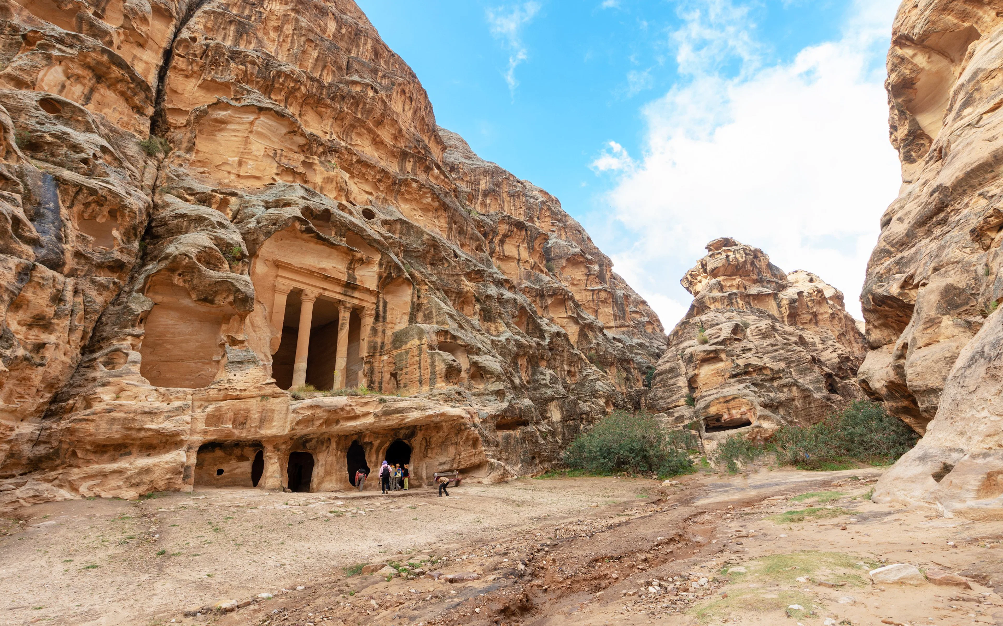 Ancient rock-cut tombs in Little Petra, Jordan, with visitors exploring the site.