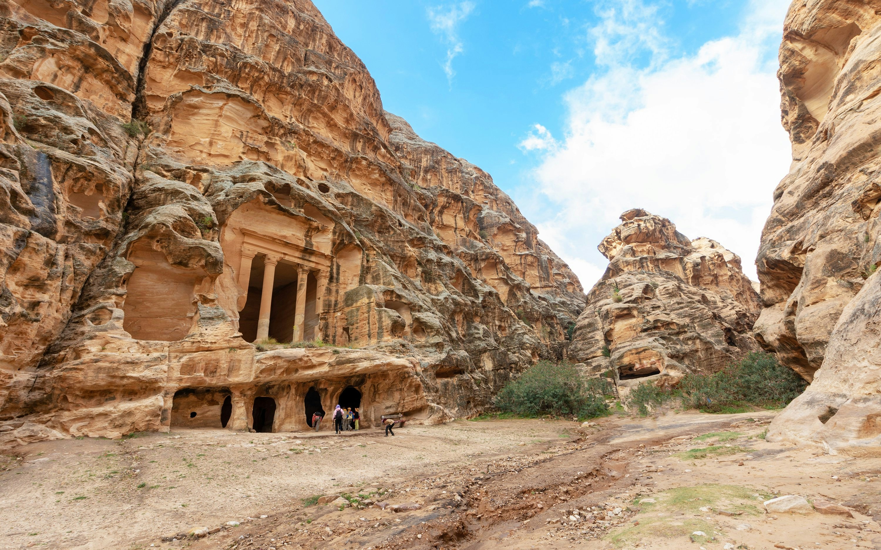 Ancient rock-cut tombs in Little Petra, Jordan, with visitors exploring the site.