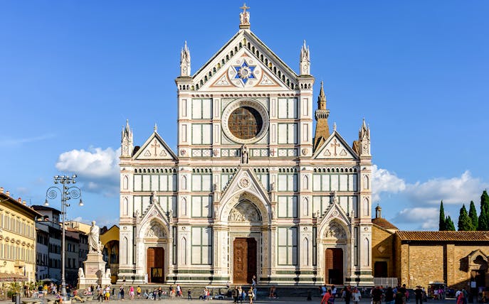 Santa Croce Basilica facade in Florence, Italy, with tourists exploring the square.