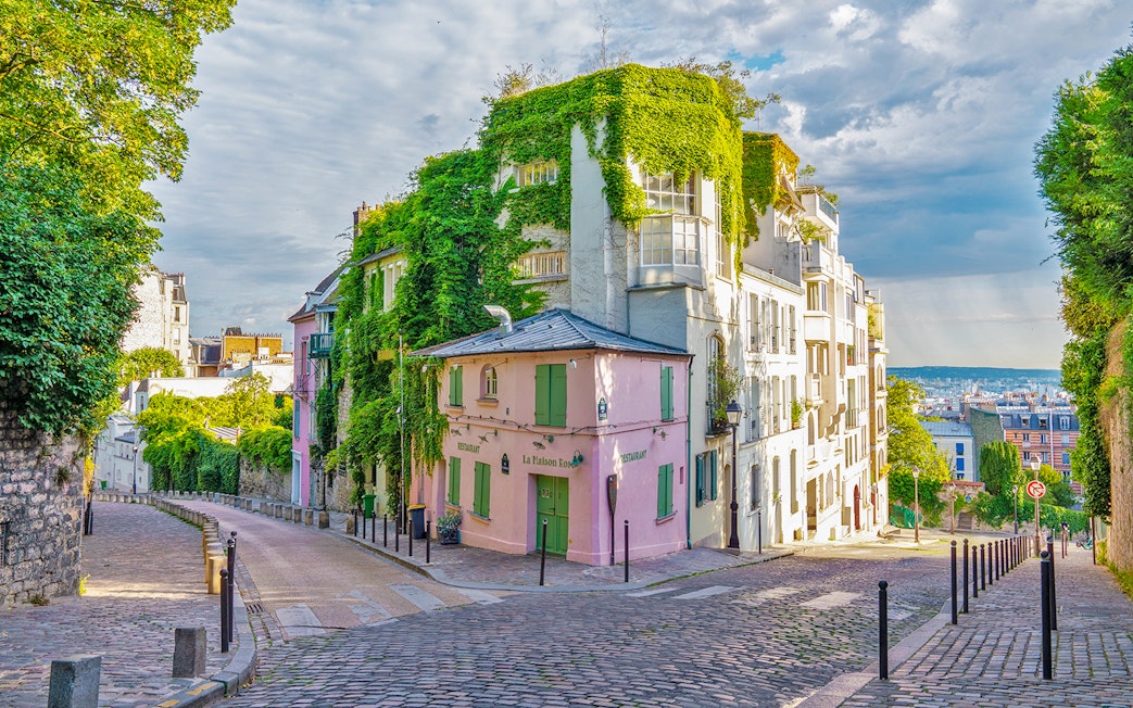 Cobbled street in Montmartre, Paris with ivy-covered buildings and a view of the city.