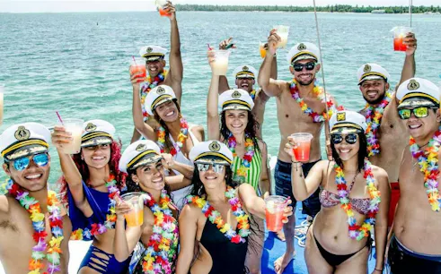 Group enjoying drinks on a party boat cruise in Punta Cana, wearing sailor hats and leis.