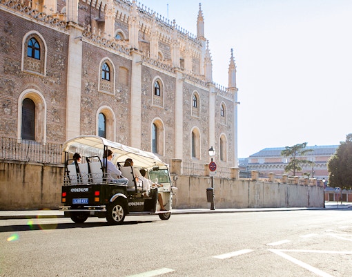 Eco Tuk Tuk tour passing historic building in Madrid.