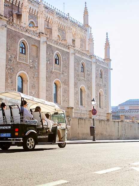 Eco Tuk Tuk tour passing historic building in Madrid.