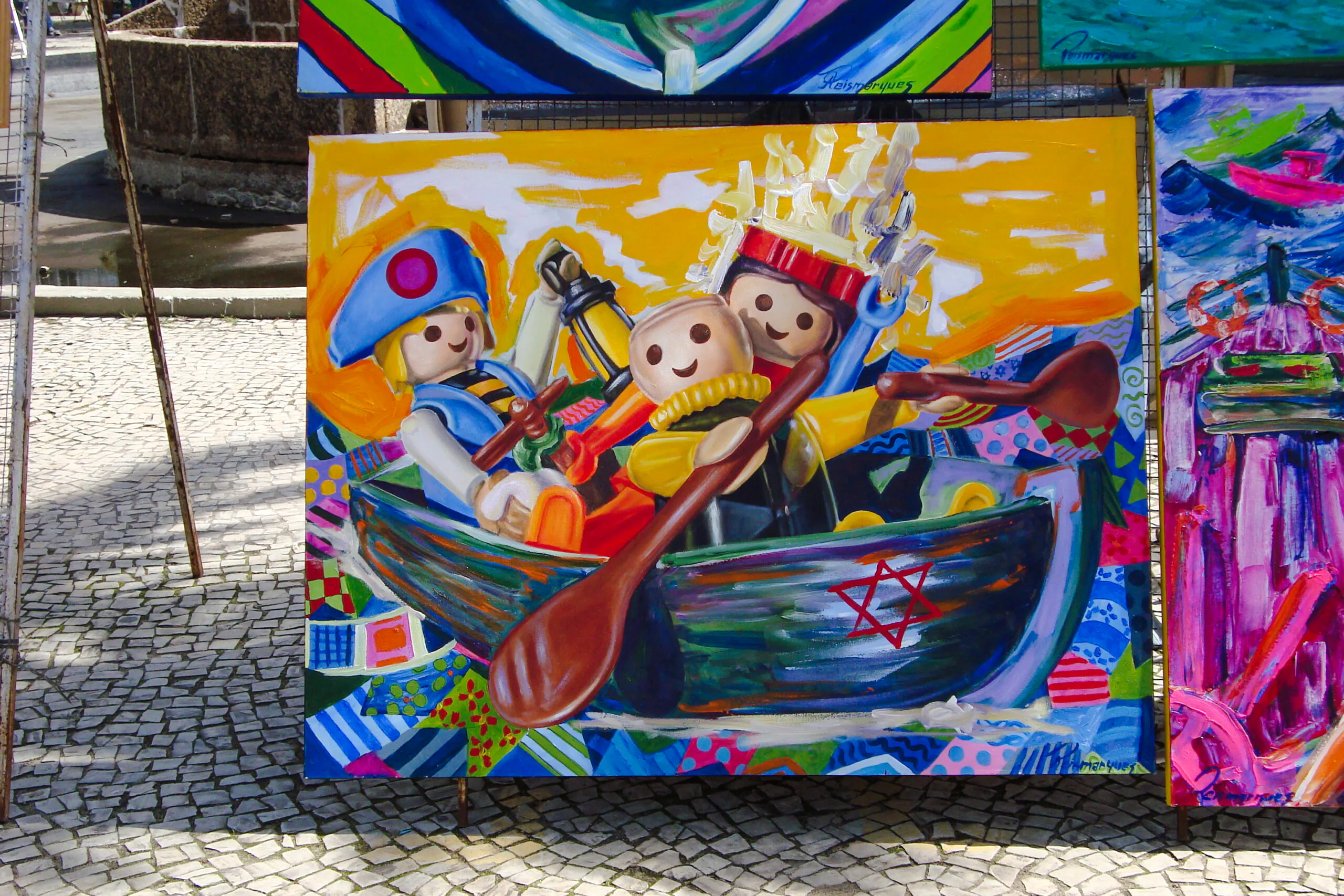 Colorful painting of toy figures rowing a boat at Ipanema Street Market, Rio de Janeiro.