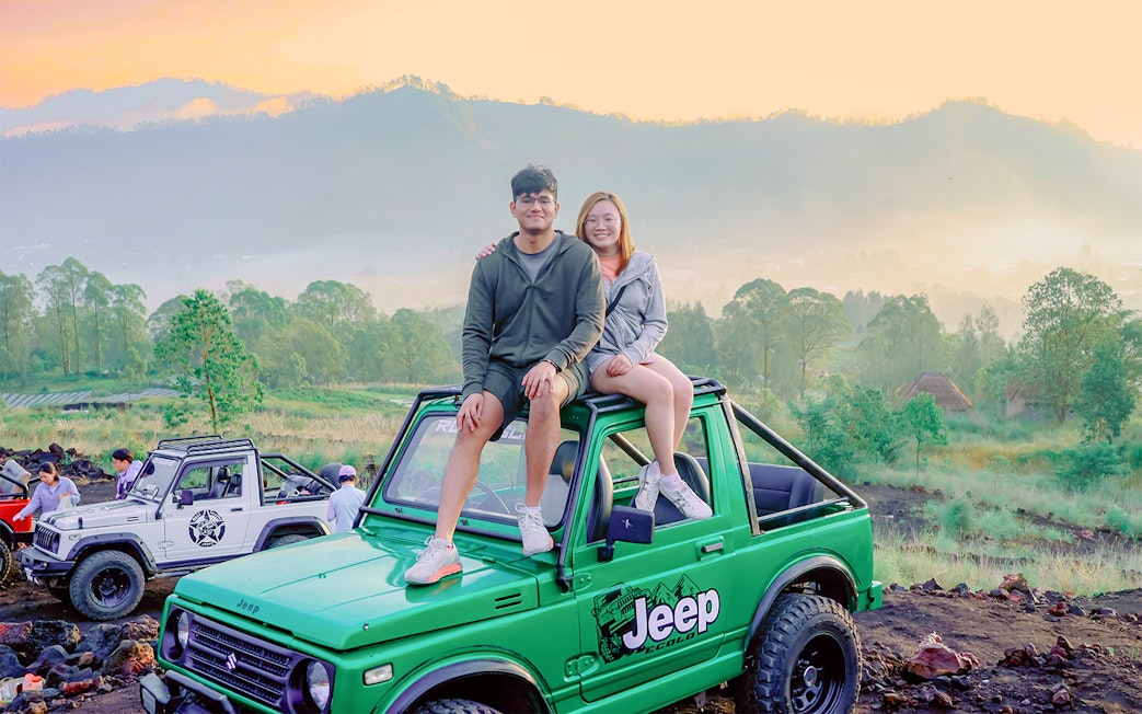 Couple sitting on a green Jeep during Mount Batur sunrise tour in Bali.