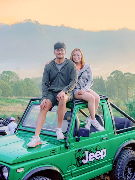 Couple sitting on a green Jeep during Mount Batur sunrise tour in Bali.