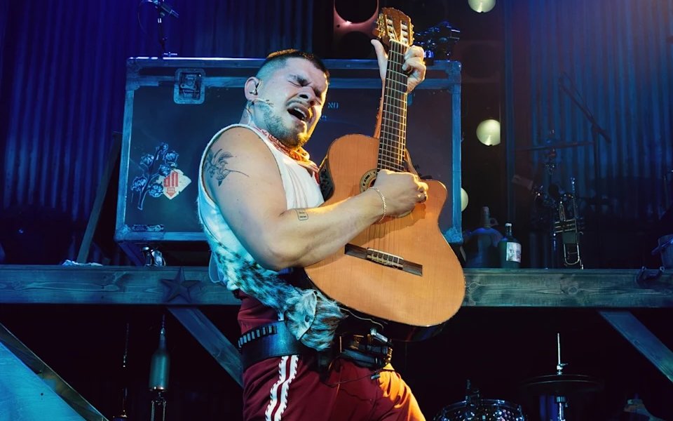 Performer playing guitar during Mexodus the Musical on Broadway stage.