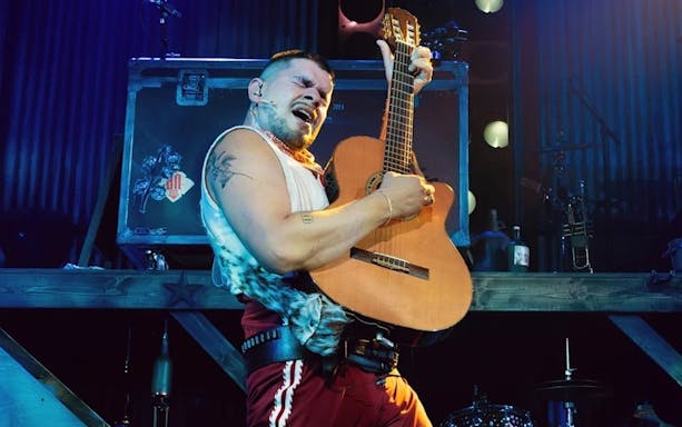 Performer playing guitar during Mexodus the Musical on Broadway stage.