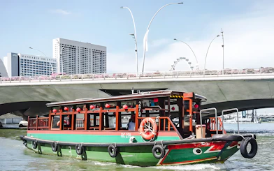 Singapore River cruise boat passing under bridge with city skyline.