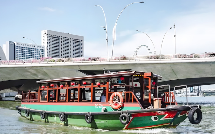 Singapore River cruise boat passing under bridge with city skyline.