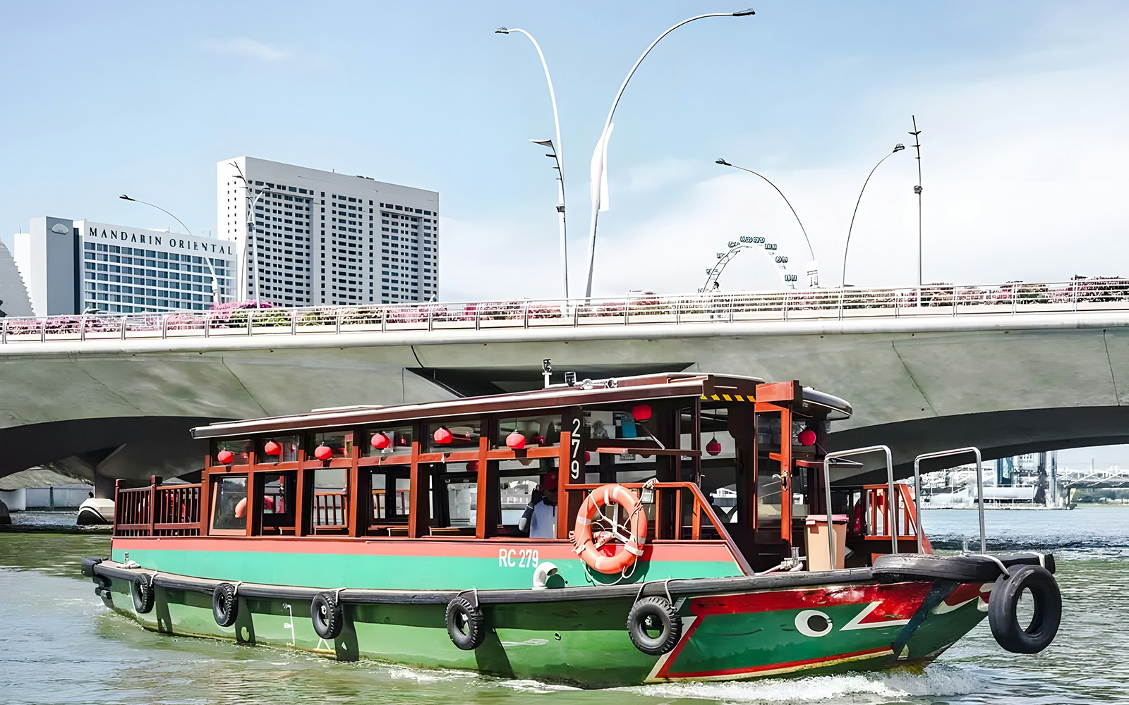Singapore River cruise boat passing under bridge with city skyline.