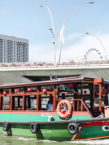 Singapore River cruise boat passing under bridge with city skyline.