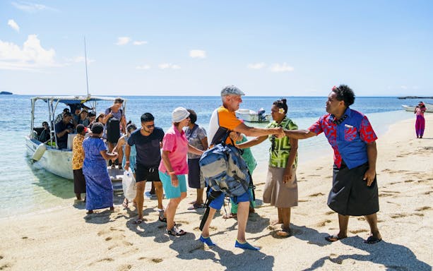 Guests arriving by boat and being greeted at a beach on a Fiji island resort.