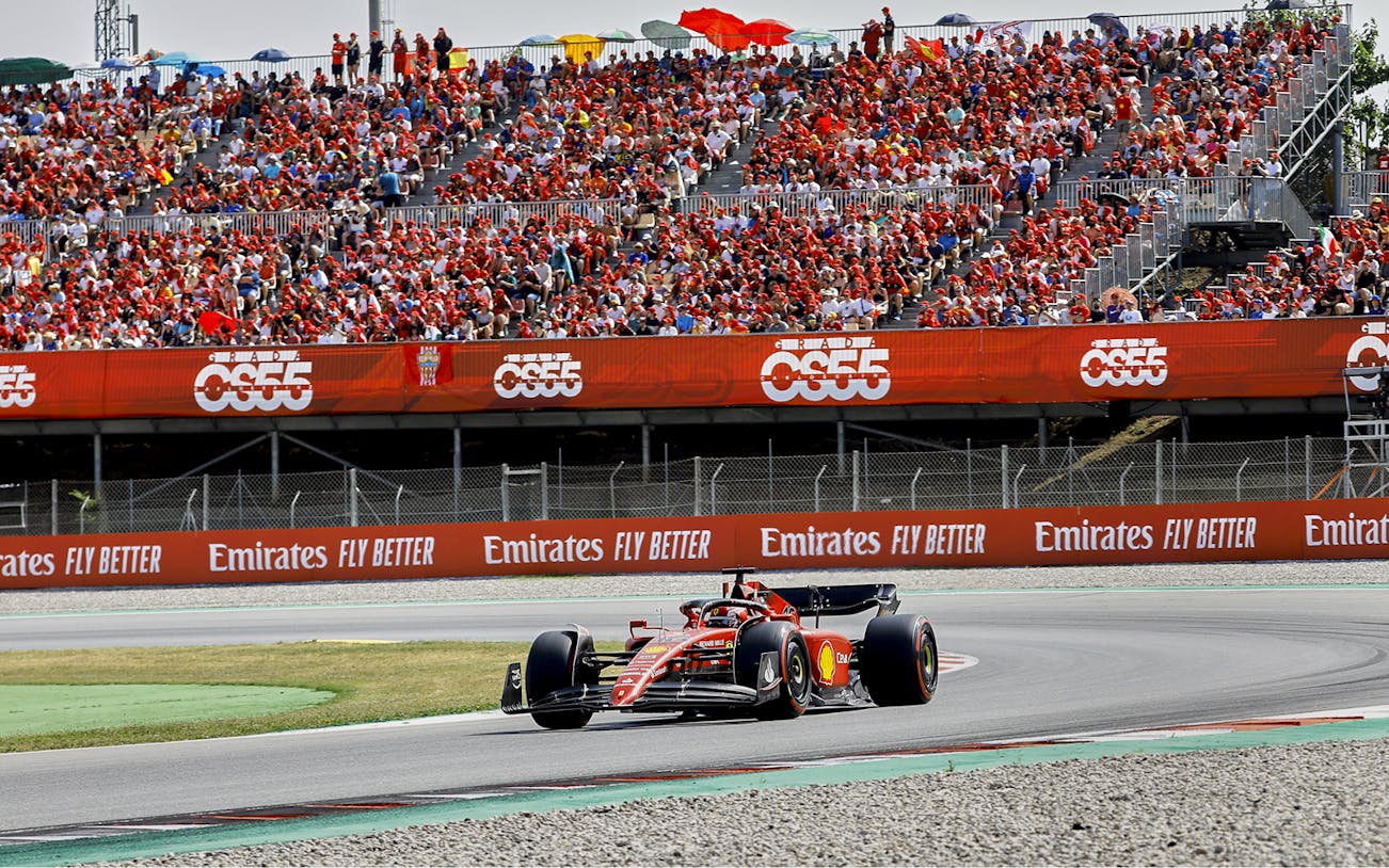 Race car on Barcelona F1 track with spectators during Grand Prix.