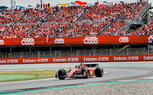 Race car on Barcelona F1 track with spectators during Grand Prix.