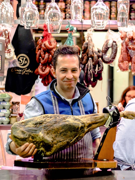 Man presenting cured ham at a tapas bar in Seville during a tasting tour.
