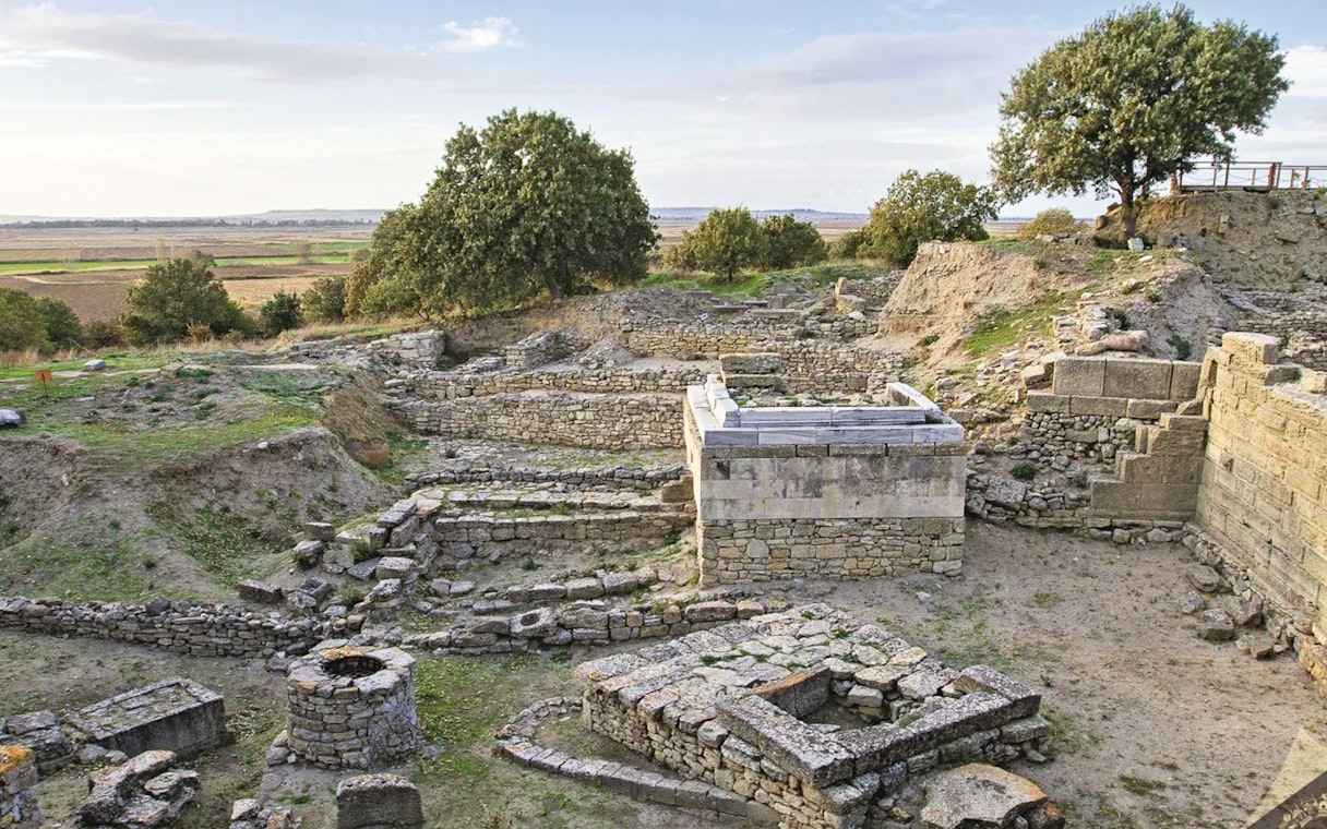 Ancient ruins of Troy with stone walls and greenery, part of a full-day tour from Istanbul.
