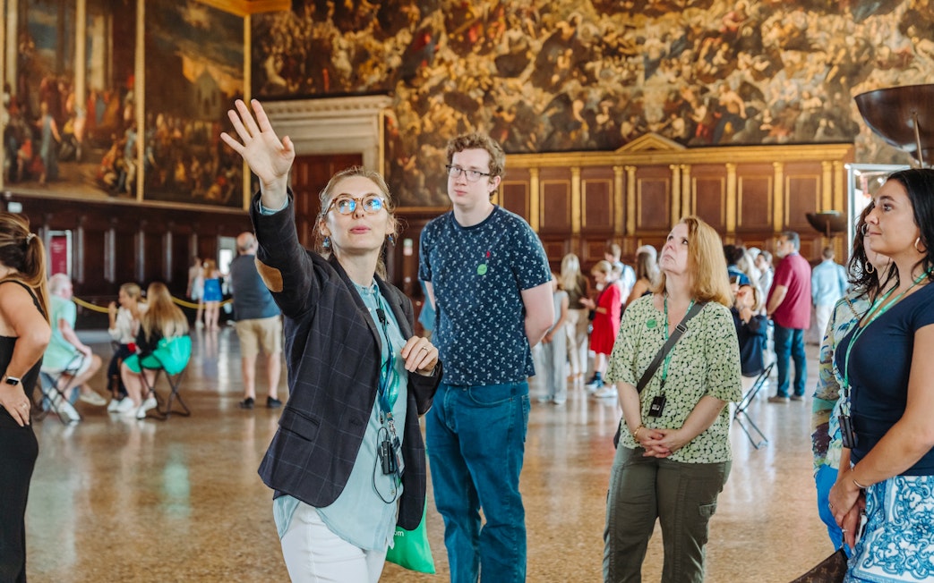 Guide leading a tour group inside Doge's Palace, Venice, with historic paintings in the background.