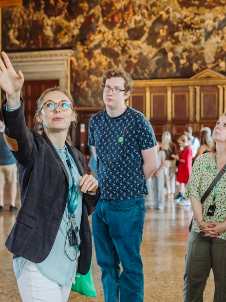 Guide leading a tour group inside Doge's Palace, Venice, with historic paintings in the background.
