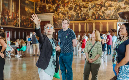 Guide leading a tour group inside Doge's Palace, Venice, with historic paintings in the background.