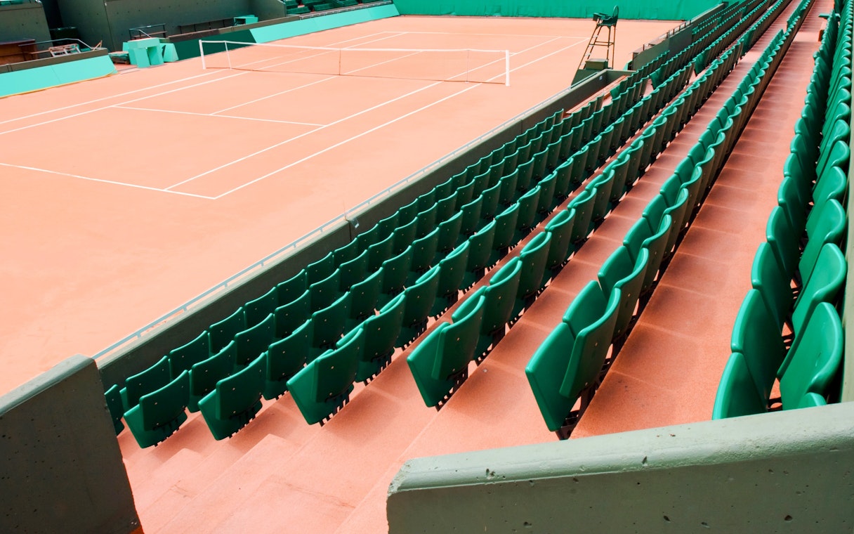 Empty clay tennis court with green seating at Roland-Garros Stadium.
