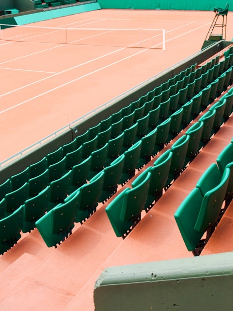 Empty clay tennis court with green seating at Roland-Garros Stadium.