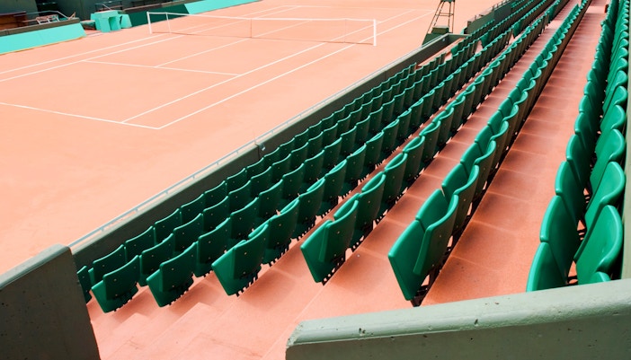 Empty clay tennis court with green seating at Roland-Garros Stadium.