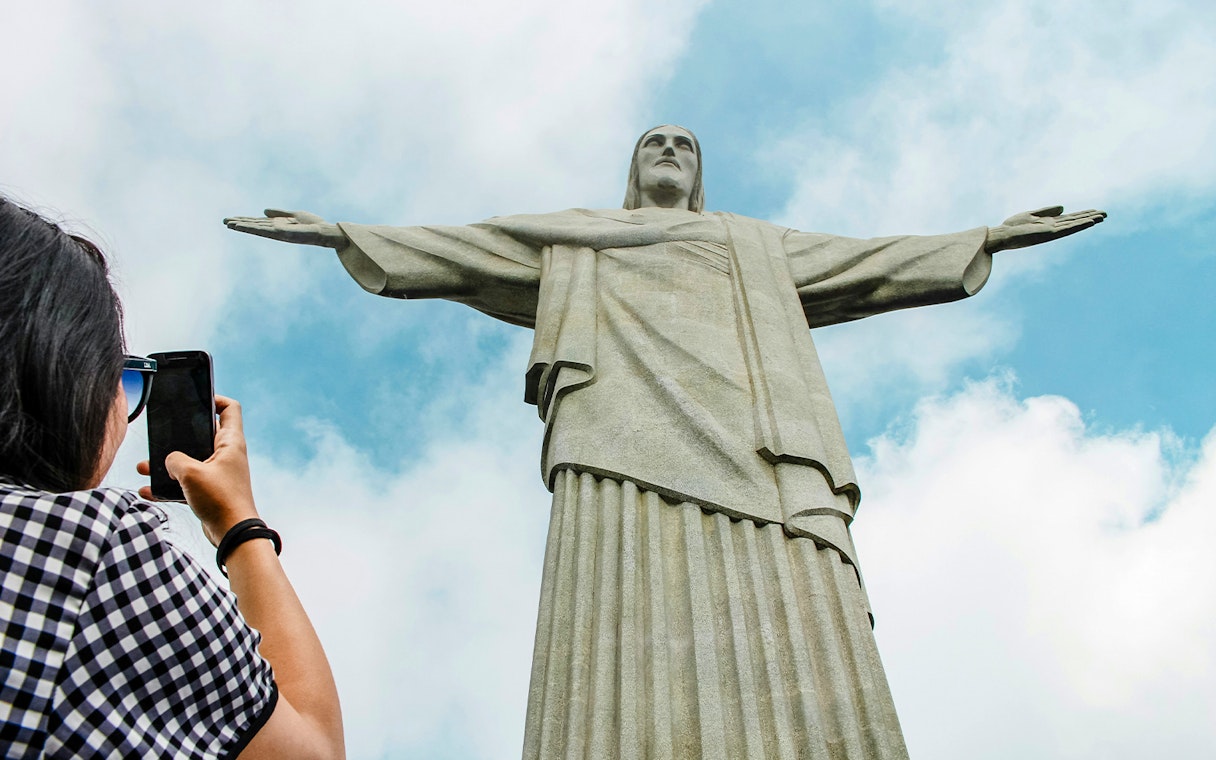 Christ the Redeemer statue in Rio de Janeiro with visitor taking photo.
